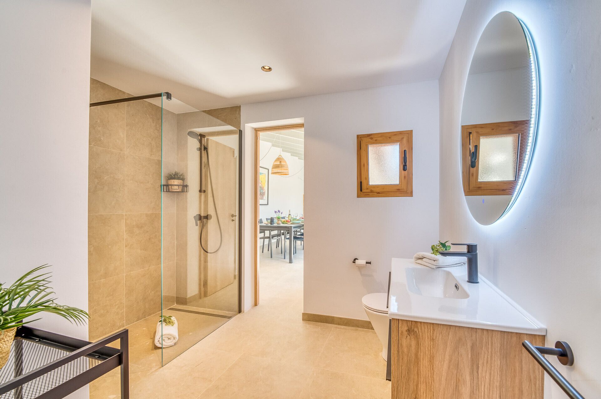 Een moderne badkamer met een douchecabine van glas, een wastafel met spiegel en uitzicht op de eetruimte.