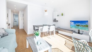 A modern living room with a sofa, dining table, chairs, a TV, and a kitchen area in the background. - Alameda 16-2 Apartment Beach-Old Town (Benidorm)