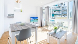 A modern living room with a dining area, large windows with a view of a building, and a flat-screen TV on the wall. - Alameda 16-2 Apartment Beach-Old Town (Benidorm)