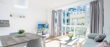 A modern living room with a dining area, large windows, and a balcony with outdoor furniture.