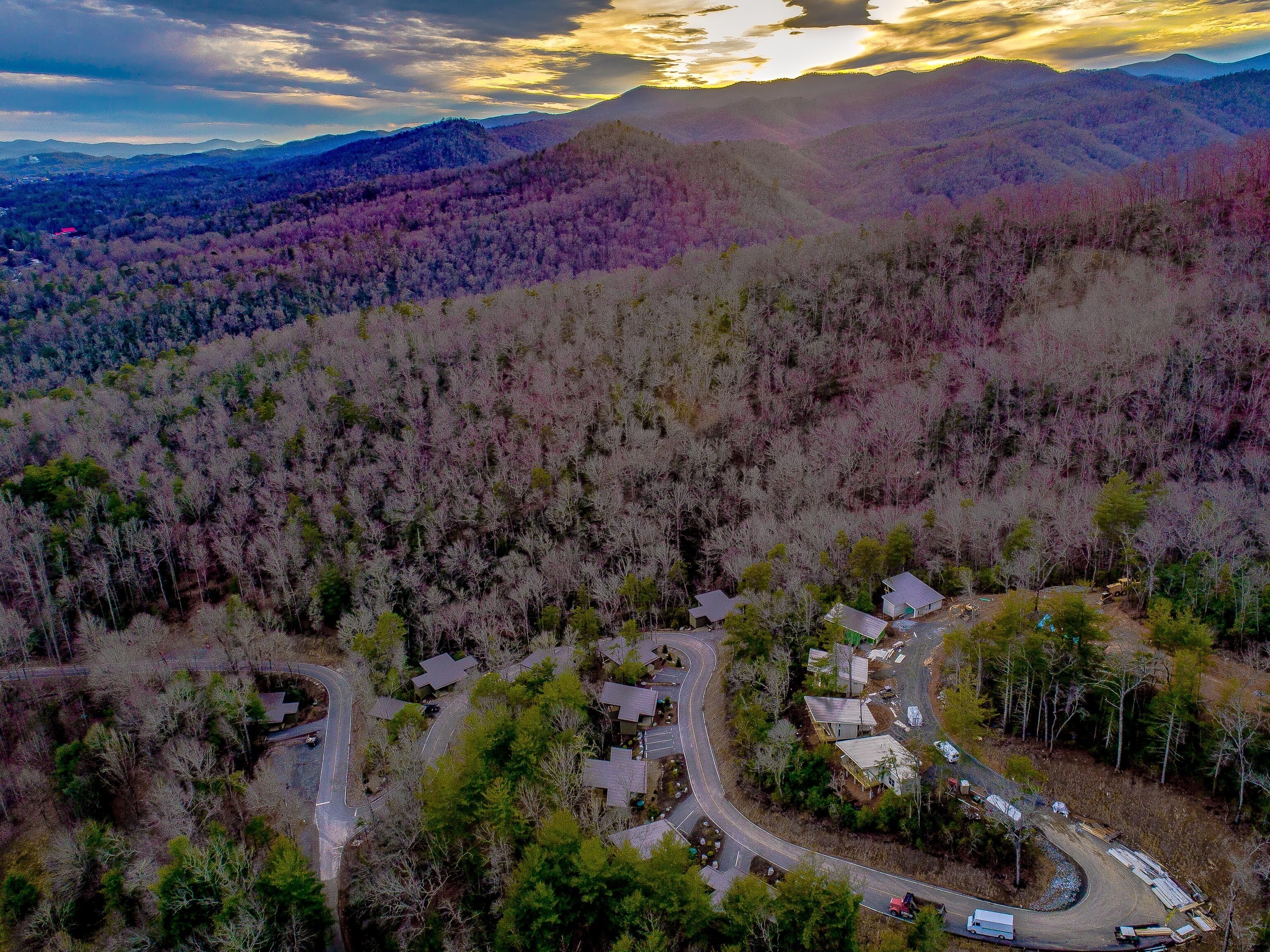 An aerial view of a residential area with houses, roads, and surrounding forested hills.