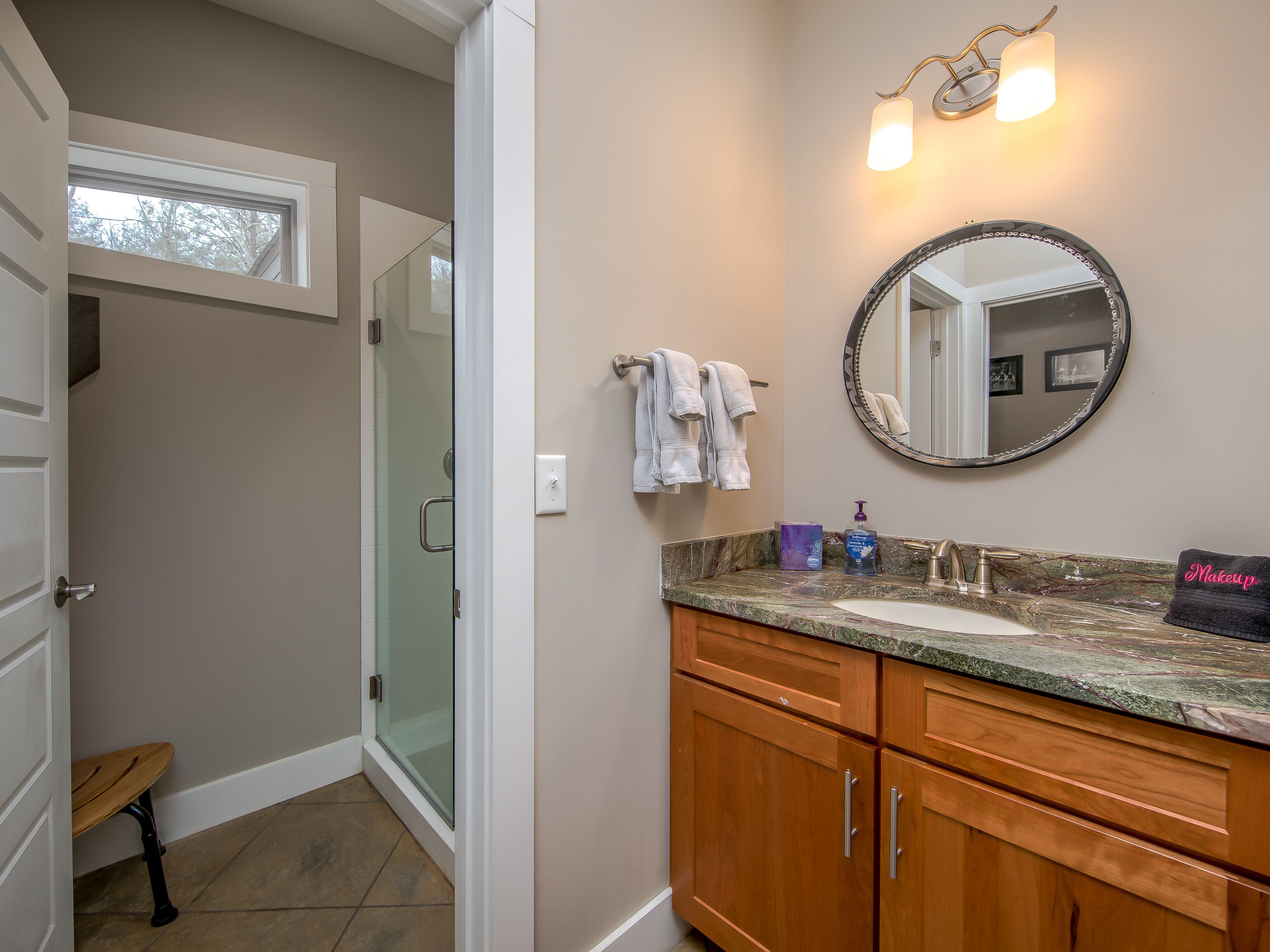 Une salle de bain comprenant un meuble-lavabo, un miroir rond, un porte-serviettes et un espace douche.