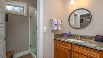 Une salle de bain comprenant un meuble-lavabo, un miroir rond, un porte-serviettes et un espace douche.