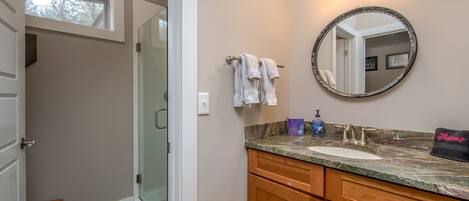 A bathroom with a vanity, a round mirror, a towel rack, and a shower area.