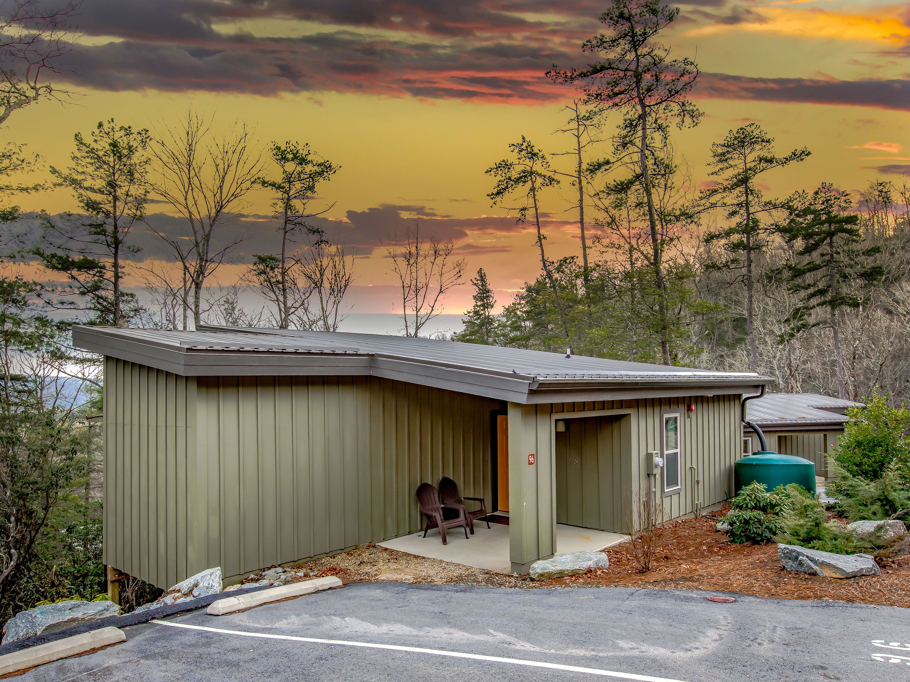 Un petit bâtiment d’un seul étage, doté d’un toit en pente, d’un porche avec deux chaises et offrant une vue sur la forêt et les montagnes environnantes.