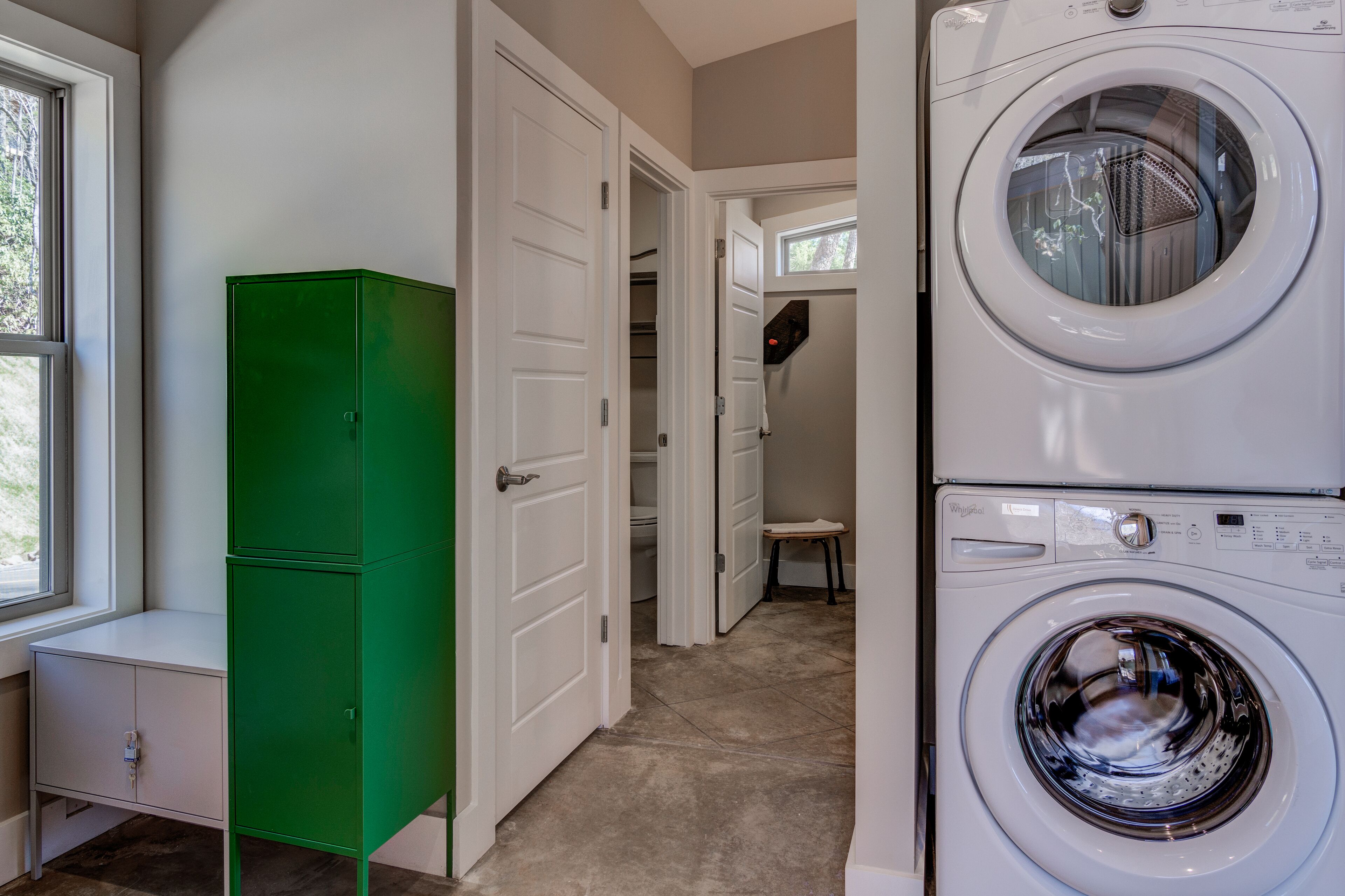 A laundry room with a stacked washer and dryer, a green utility cabinet, and a window providing natural light.