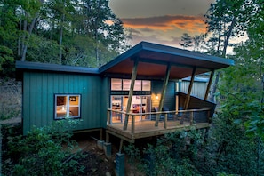 A modern house with a wooden deck, large windows, and a staircase leading to an upper level. - Pilot Cove Forest Lodging (Pisgah Forest)