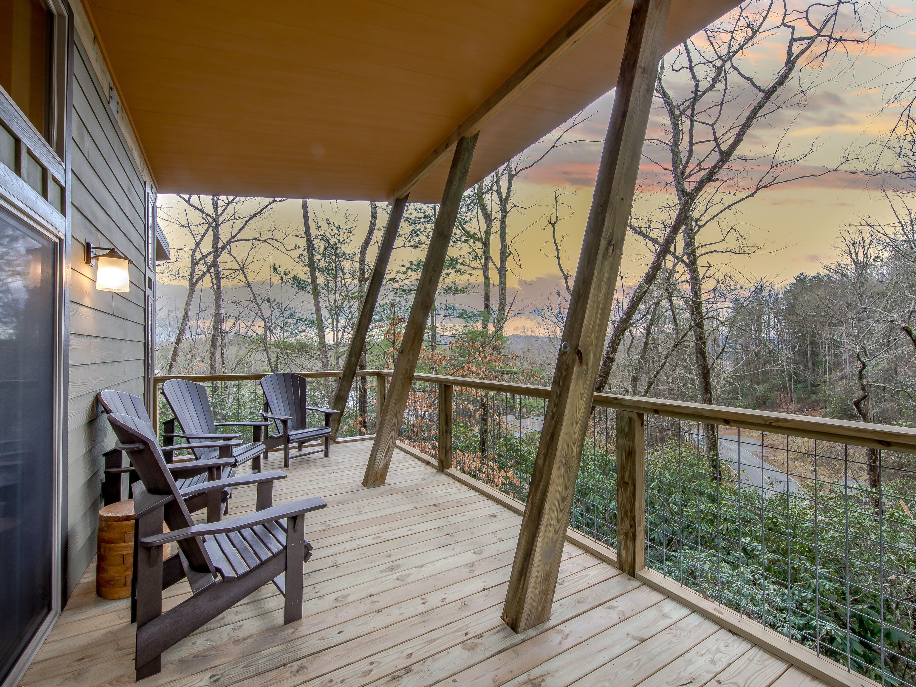 A wooden deck with two Adirondack chairs and a wooden bench, overlooking a forested area.