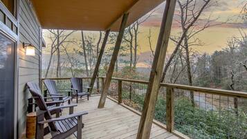 A wooden deck with two Adirondack chairs and a wooden bench, overlooking a forested area.