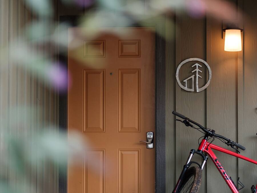 A red bicycle leaning against a wooden door with a mailbox and a light fixture above it.
