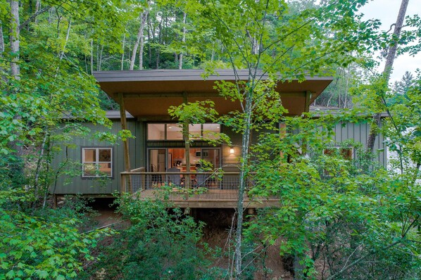 A cabin with a deck, surrounded by dense forest. - Pilot Cove Forest Lodging (Pisgah Forest)