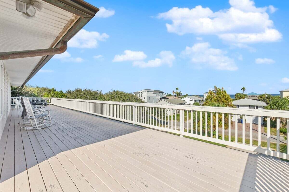 Eine Holzterrasse mit weißer Brüstung, mit Blick auf eine Wohngegend mit Häusern und Bäumen.