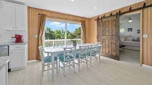 A kitchen with white cabinets, a dining table with chairs, a red coffee maker, and a view of greenery outside.