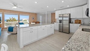 A modern kitchen with white cabinetry, a stainless steel refrigerator, and a large island with a granite countertop.