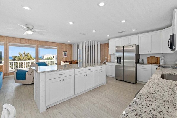 A modern kitchen with white cabinetry, a stainless steel refrigerator, and a large island with a granite countertop.