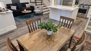 Eine moderne Küche mit Edelstahlgeräten, ein Essbereich mit Holztisch und Stühlen sowie eine Treppe, die in ein Obergeschoss führt.