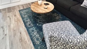 Ein modernes Wohnzimmer mit Kamin, einem flachbildfernseher darüber, einem dunkelgrauen Sofa und einem gemusterten Teppich.