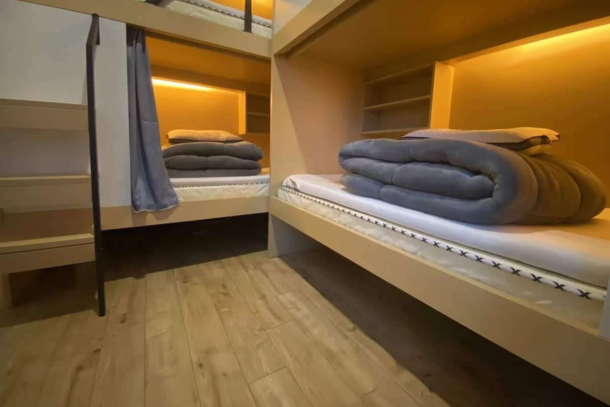 A dormitory-style room with bunk beds, wooden flooring, and a warm ambient light.