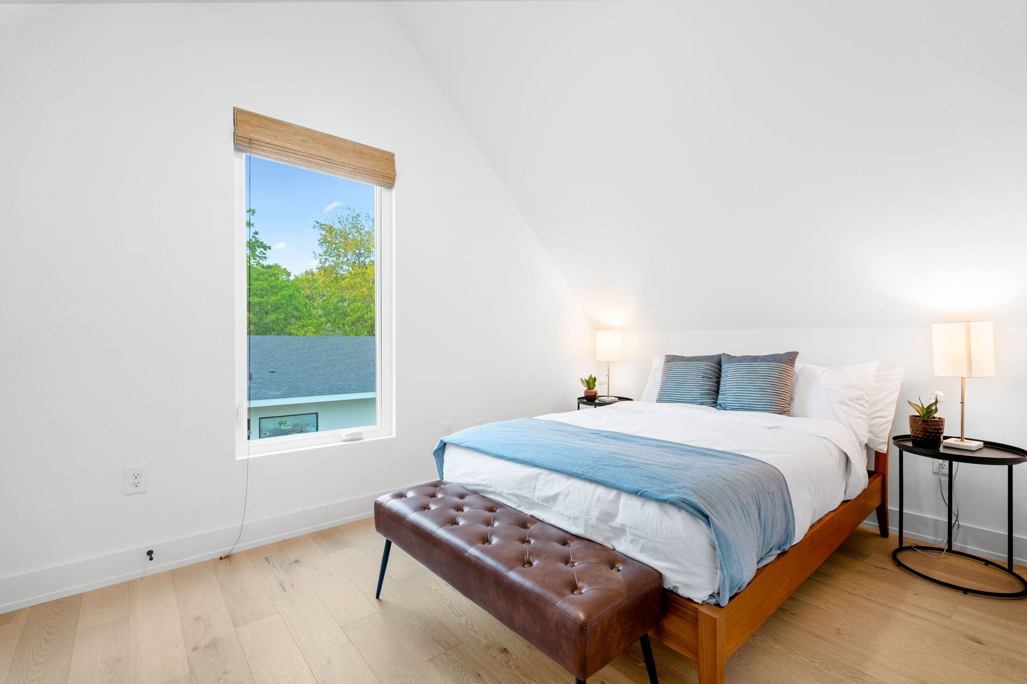 A bedroom with a bed, bench, bedside tables, and a window with a view.