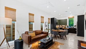 A modern living room with a brown leather sofa, a coffee table, and a dining area with a table and chairs. - Stylish 2 Bedroom Retreat in South Austin (Austin)