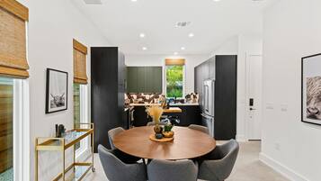 A modern kitchen with dark cabinets, a central island, and a dining area with a round table and chairs.