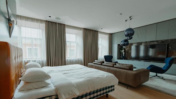 A modern hotel room with a large bed, a sofa, a TV, and a window with curtains. - Luxury apartments 3 (Vilnius)