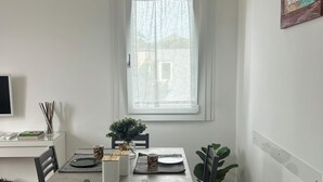 Comedor con una mesa dispuesta para cuatro personas, sillas, una ventana con vistas, un cuadro en la pared y una planta en el alféizar.