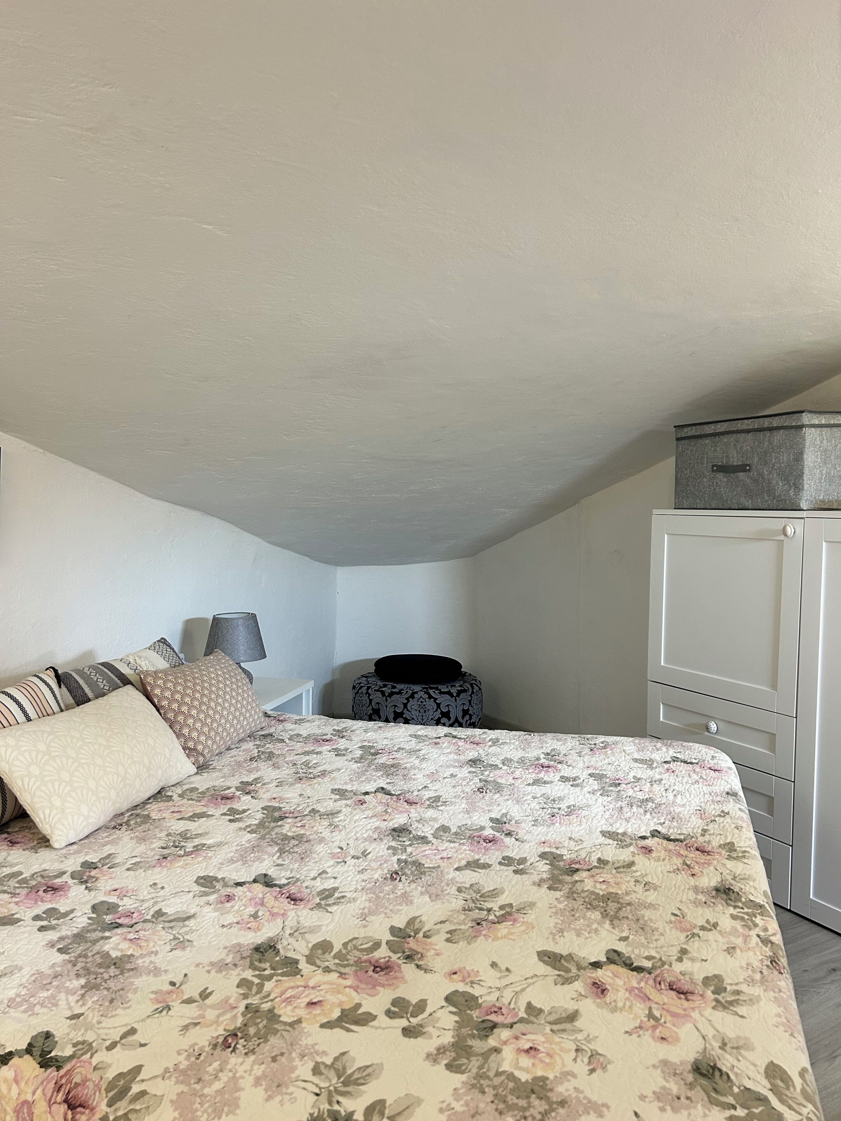 A bedroom with a bed, pillows, a lamp, a dresser, and a suitcase.