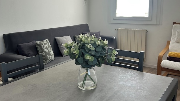 Una sala moderna con un sofá gris, una mesa de comedor y un jarrón de flores.