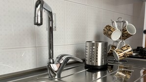 Un lavamanos de acero inoxidable con un grifo moderno, un recipiente metálico perforado y un escurreplatos con tazas decoradas.