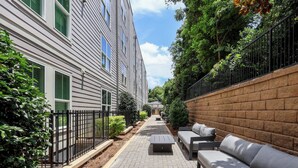 A courtyard with a brick pathway, outdoor seating, and a building with green shutters.