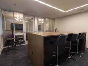 A modern conference room with a wooden table, bar stools, and a glass partition.