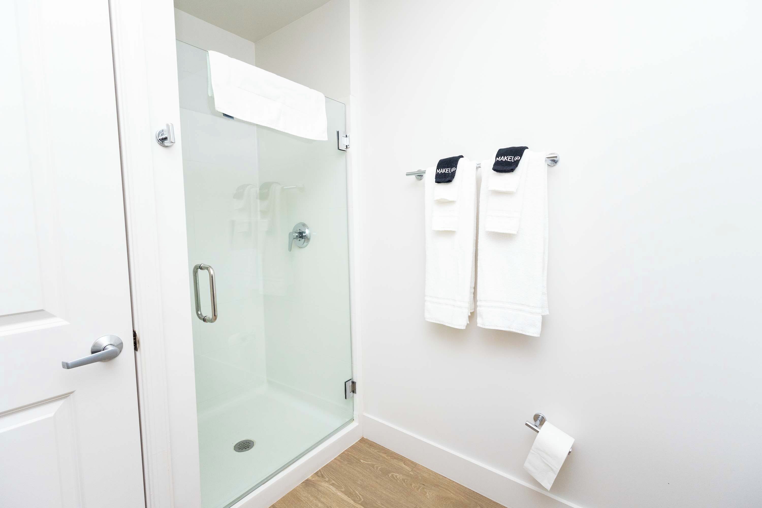 A bathroom with a glass-enclosed shower, white towels, and a toilet paper holder.