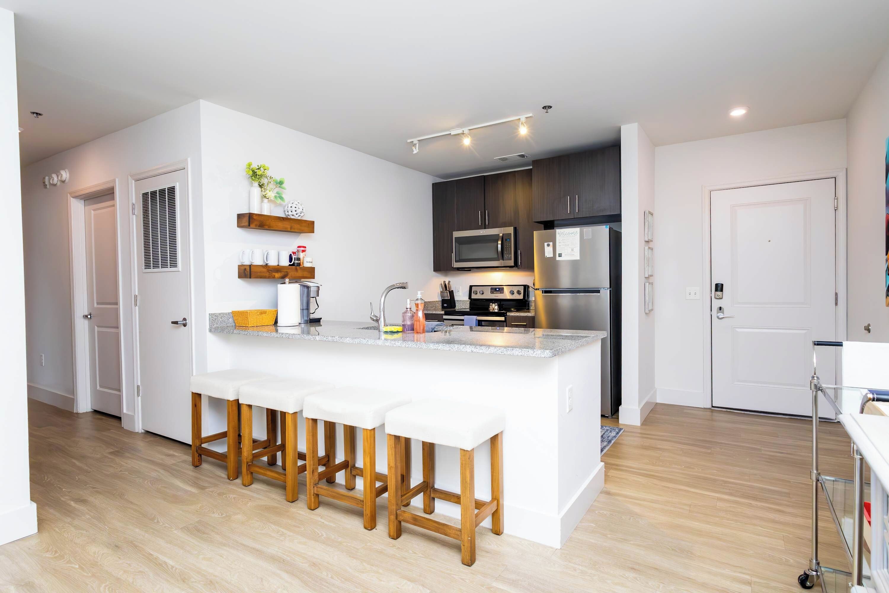 A modern kitchen with a central island, bar stools, a microwave, a refrigerator, and wooden cabinets.