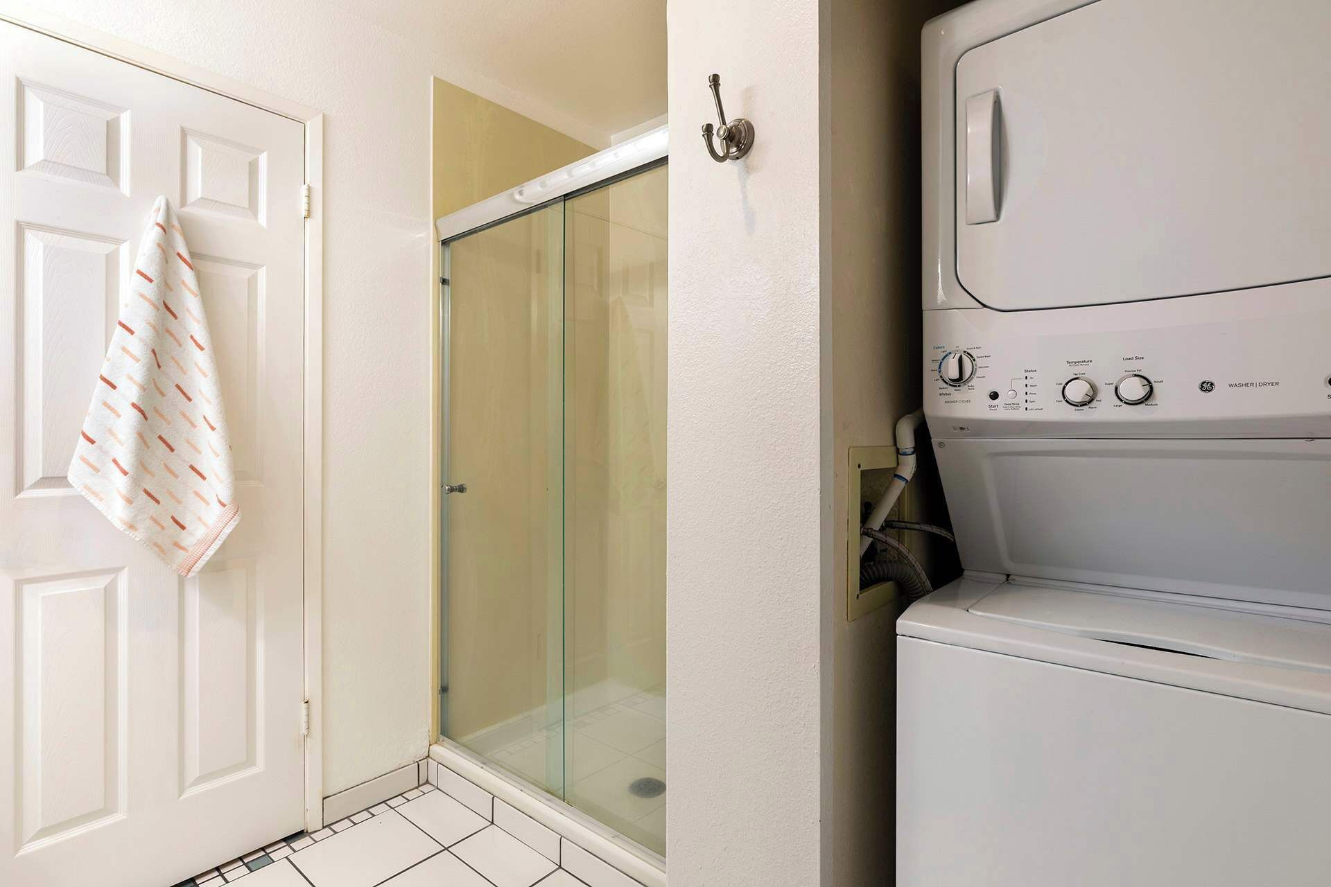 A laundry area with a washing machine and dryer, a glass shower door, and a towel hanging on a door.