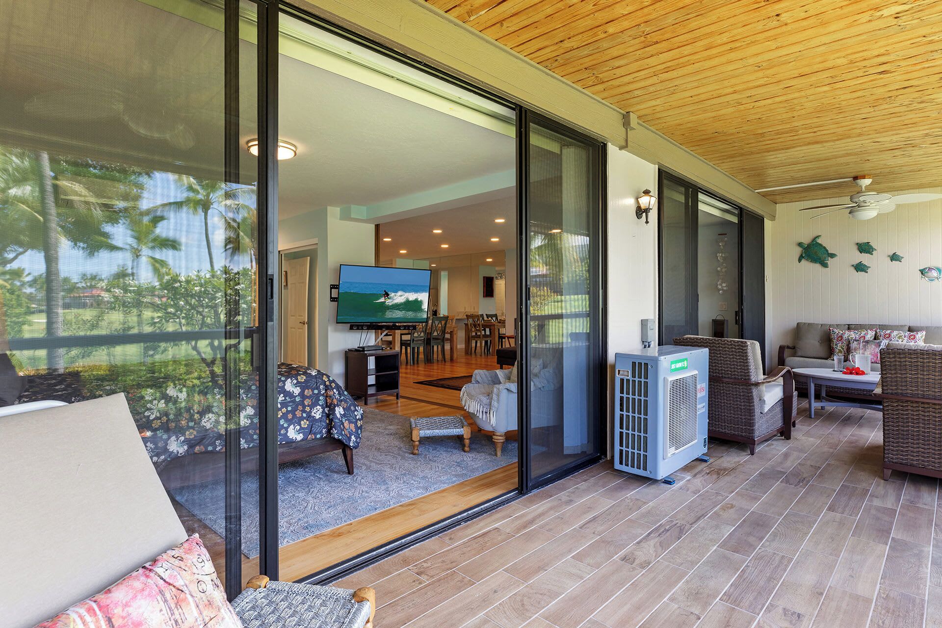 A spacious living area with a large sliding glass door leading to a balcony, furnished with a sofa, chairs, and a TV.