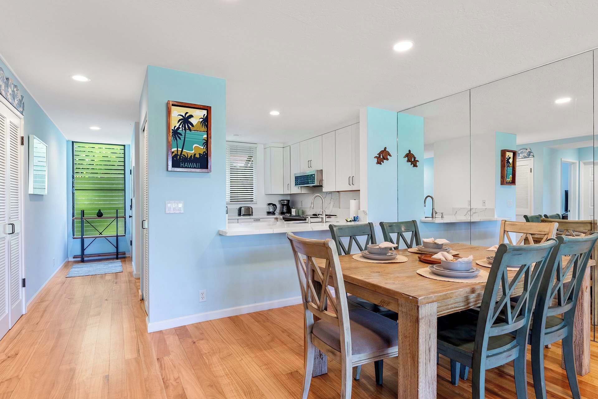 A modern kitchen with white cabinets, a wooden dining table, and teal chairs.