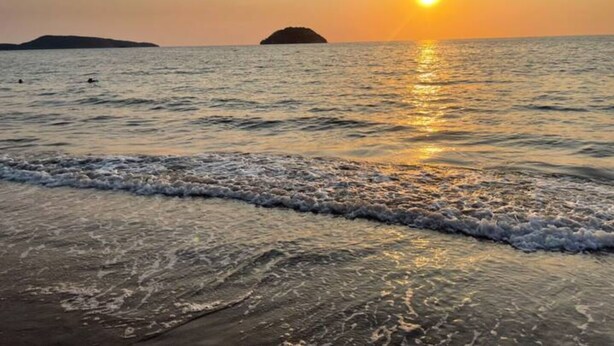 A beach at sunset with calm waves and a distant island.