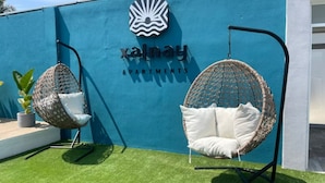 Two hanging chairs with cushions against a blue wall with a logo and the text "xalnay APARTMENTS".