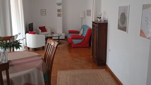 A living room with a dining area, a red sofa, a white armchair, and a wooden cabinet. - Acropolis penthouse with breathtaking city view (Athina)