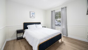 Ein ordentlich eingerichtetes Schlafzimmer mit Bett, Nachttisch und einem Fenster mit Vorhängen.