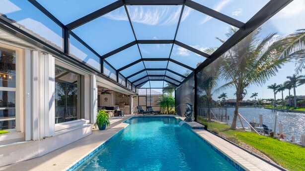 A swimming pool with a glass enclosure, surrounded by a patio area with outdoor furniture and a view of a body of water. - Luxury Tropical long waterfront view w/bikes,kayaks,golf clubs,beach gear incl. (Punta Gorda)