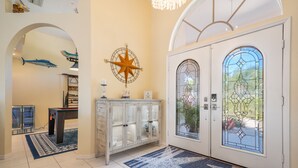 A spacious foyer with a large arched doorway, a decorative compass wall piece, and a stained glass window. - Luxury Tropical long waterfront view w/bikes,kayaks,golf clubs,beach gear incl. (Punta Gorda)