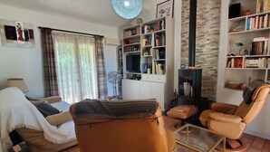 Un soggiorno con divano, poltrona reclinabile, tavolino in vetro, libreria, camino e ventilatore.