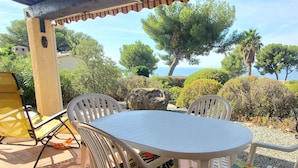 Patio esterno con tavolo rotondo e sedie bianche, immerso nel verde e con vista sul mare.