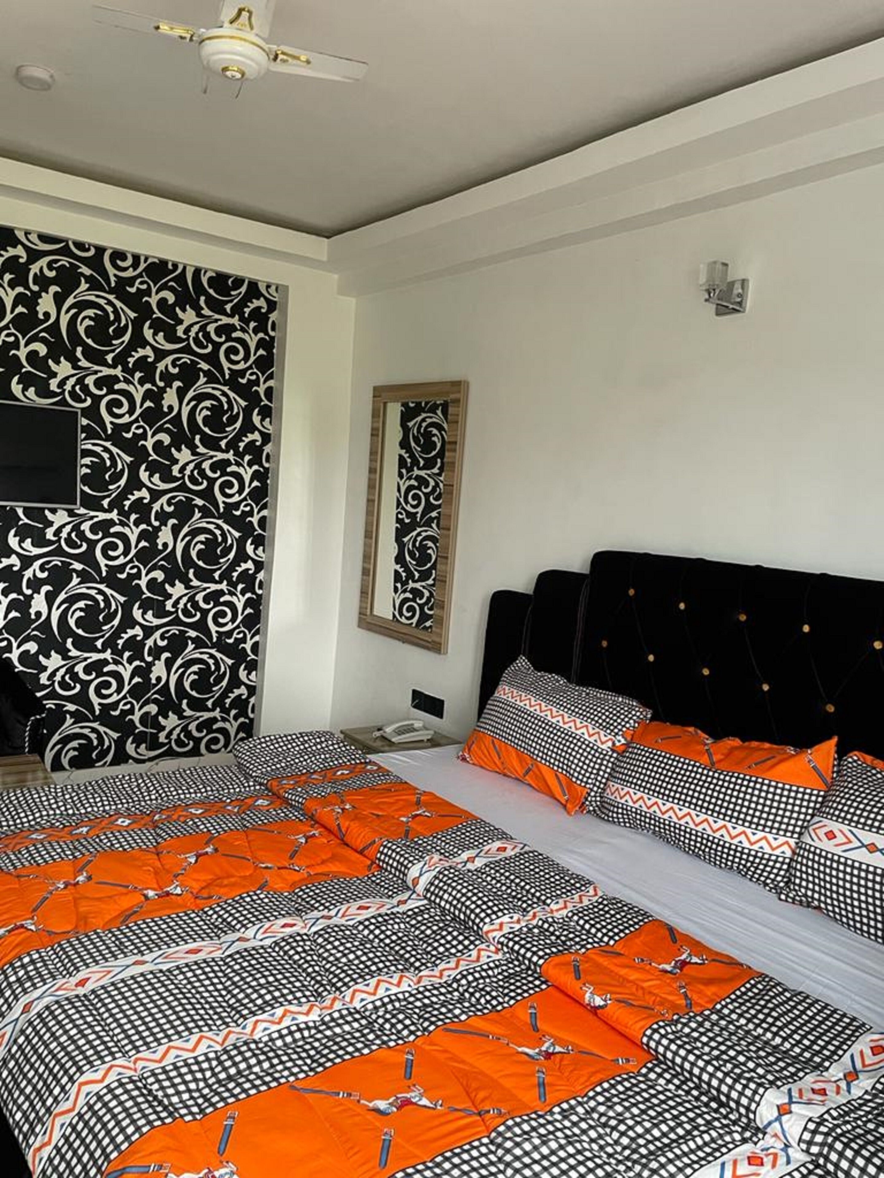 A bedroom with a black and white patterned wall, a bed with orange and black bedding, and a ceiling fan.