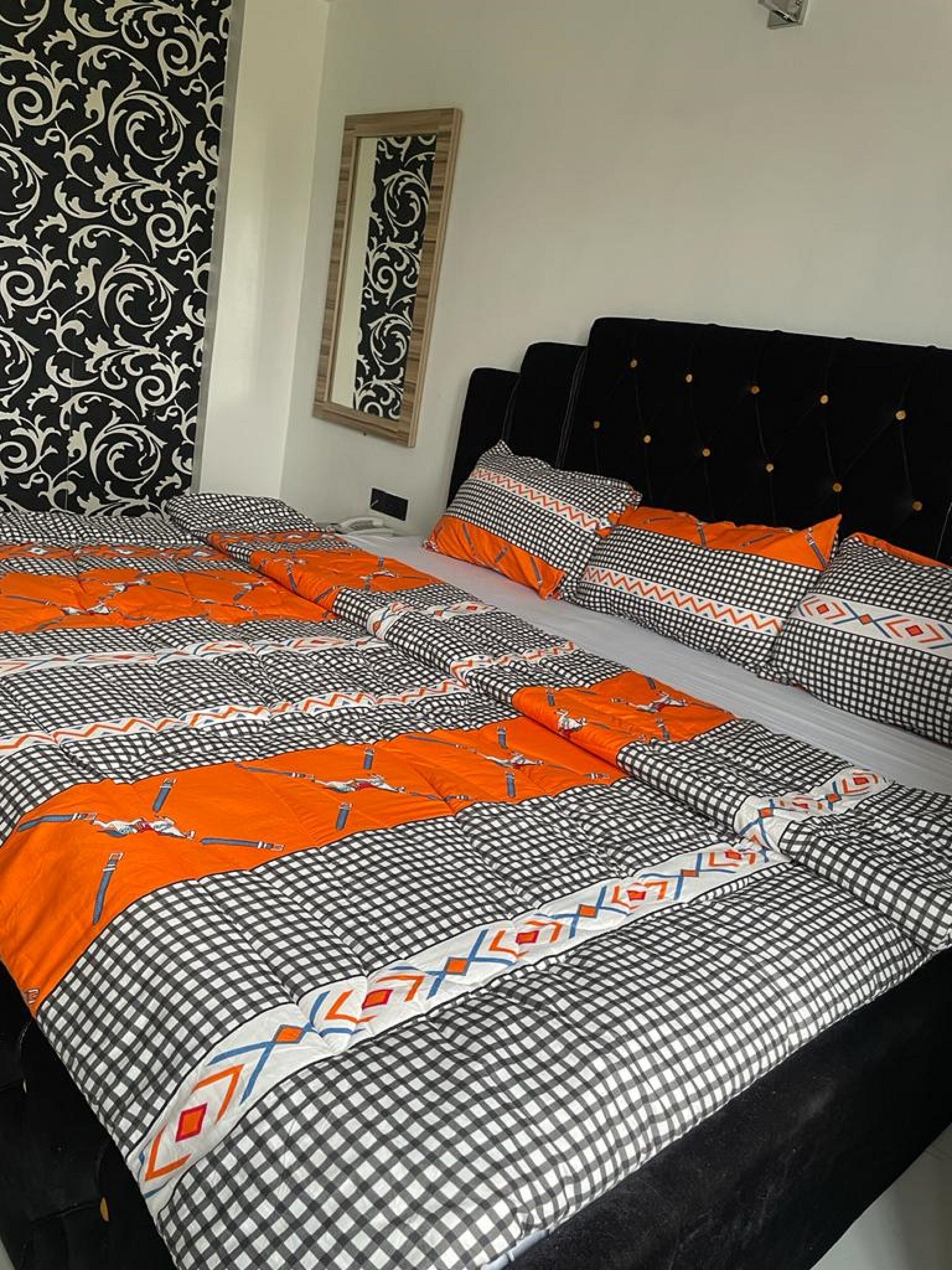 Habitación de hotel con una cama grande, cabecero negro y pared con diseño.