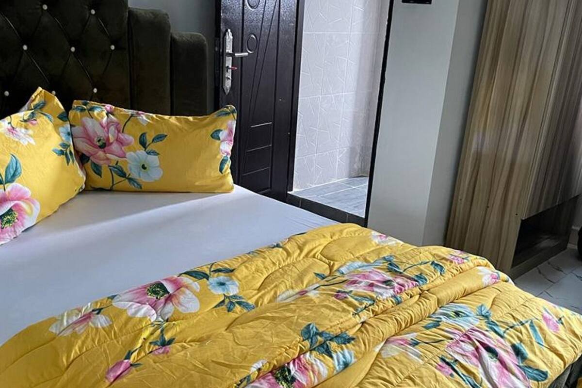 A bedroom with a bed, a dark upholstered headboard, a door with a geometric pattern, and a window with curtains.