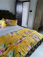 Un dormitorio con cama, cabecera tapizada oscura, puerta con diseño geométrico y ventana con cortinas.