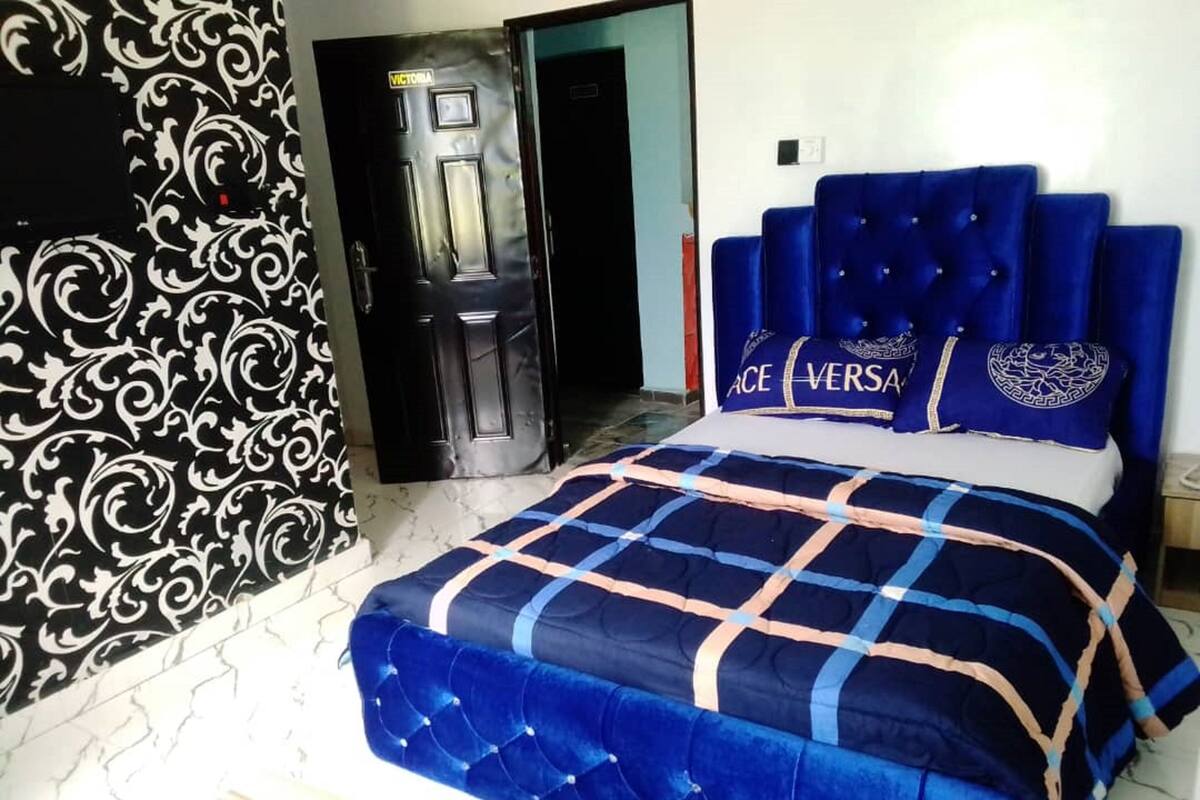 A bedroom with a bed, a patterned wall, and a door labeled "VICTORIA".